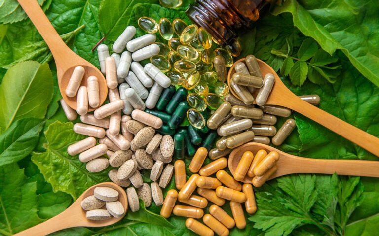 Capsules herb supplements on green leaves background. Selective focus.